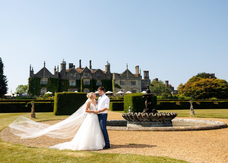 A bride and groom posing in front of Eastwell Manor, captured by a talented Kent wedding photographer.