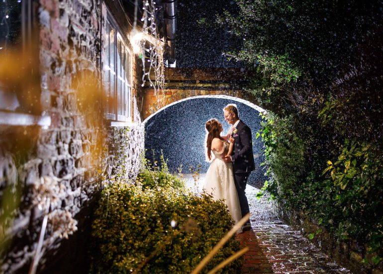 A Sussex Wedding Photographer captures a bride and groom's romantic moment under a bridge in the rain.