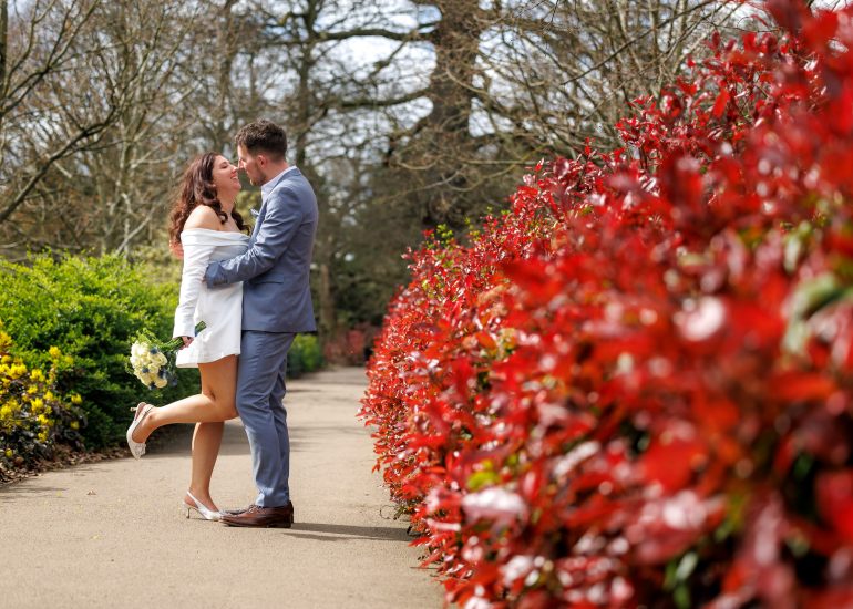 Lindsey and Billy embracing on a path lined with red flowers at Danson House.