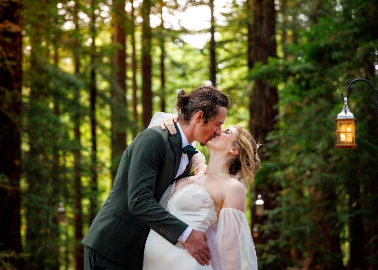 A couple in wedding attire shares a tender kiss in the serene beauty of Two Woods Estate, with a lantern hanging nearby, perfectly captured by wedding photography.