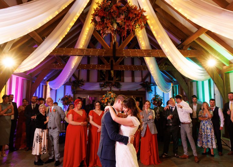 A bride and groom share their first dance in a decorated barn, surrounded by their wedding party and guests in formal attire, perfectly captured with Brookfield Barn Wedding Photography.